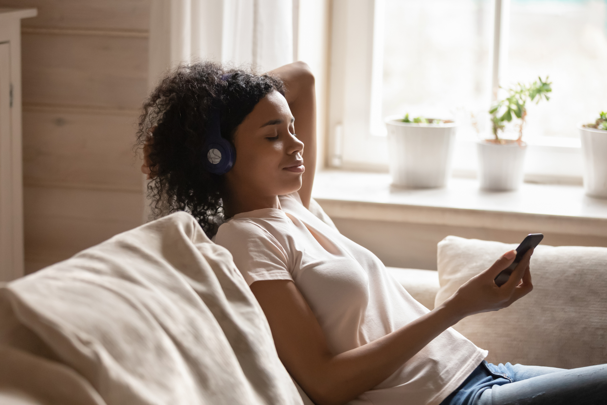 African woman wearing headphones listen music use phone resting indoors